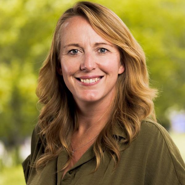 Smiling woman with wavy blonde hair and green shirt outdoors.