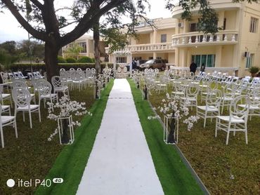 Elegant outdoor wedding setup with white chairs and floral decorations along the aisle.
