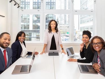 Diverse professionals in a bright office meeting, smiling and engaged with laptops.