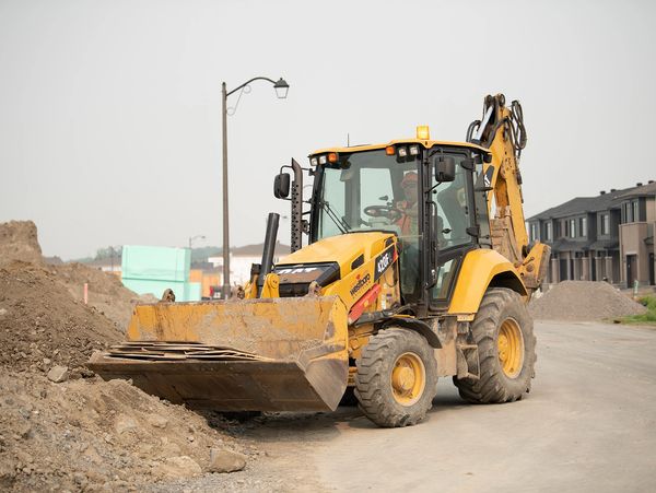 Yellow backhoe loader working on a construction site near houses.