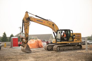 A yellow excavator with a construction worker inside on a construction site.