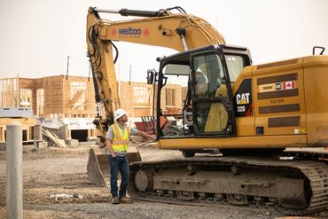 Construction worker standing by a large excavator at a building site.