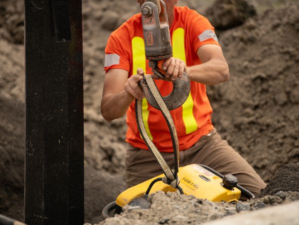 Construction worker securing a heavy hook on equipment at a site.
