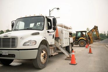 Utility truck and backhoe at a construction site with safety cones.