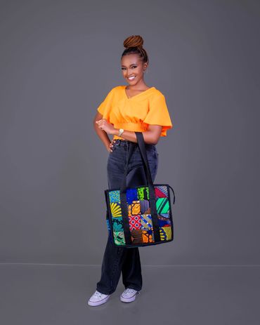 Smiling woman in orange top holding a colorful patchwork bag against a gray background.