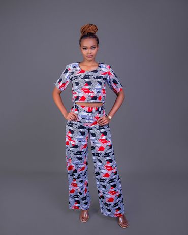 Woman posing in a colorful patterned two-piece outfit with braided hair in a bun.