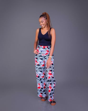 Smiling woman in black top and colorful patterned pants against gray background.