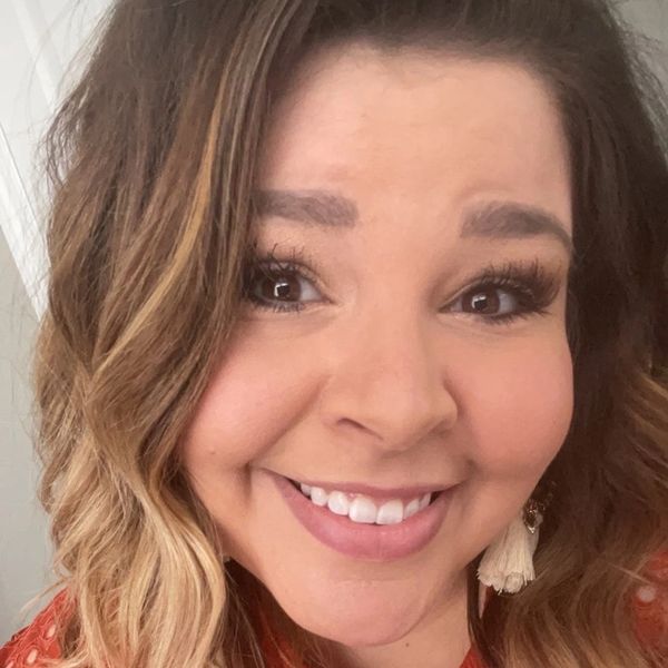 Smiling woman with ombre hair wearing a textured orange top.