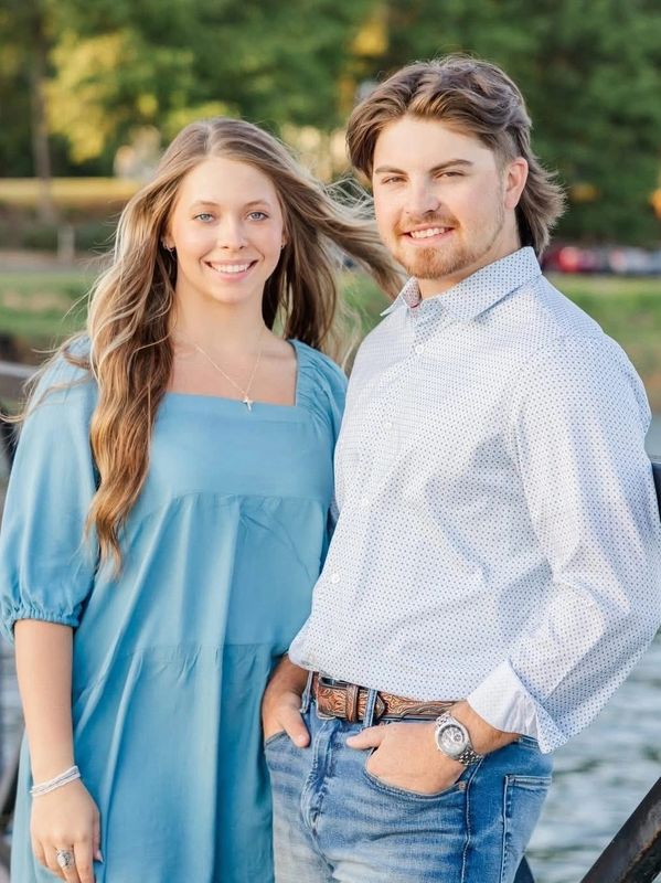 A smiling young couple stands outdoors by the water, enjoying a sunny day.