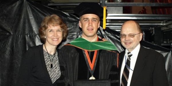 Graduate with family at commencement ceremony.