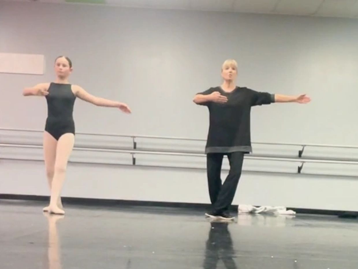 A ballet student and instructor practicing dance positions in a studio.