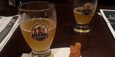 Two glasses of beer and a small dog-shaped figurine on a table.