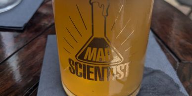 A glass of beer with foam on top, labeled with a Mad Scientist logo.