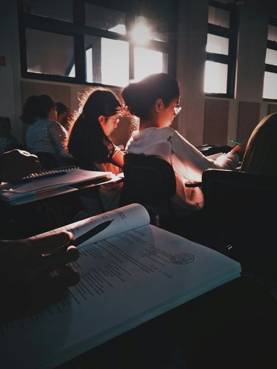 Students studying in a sunlit classroom with notebooks and pens.