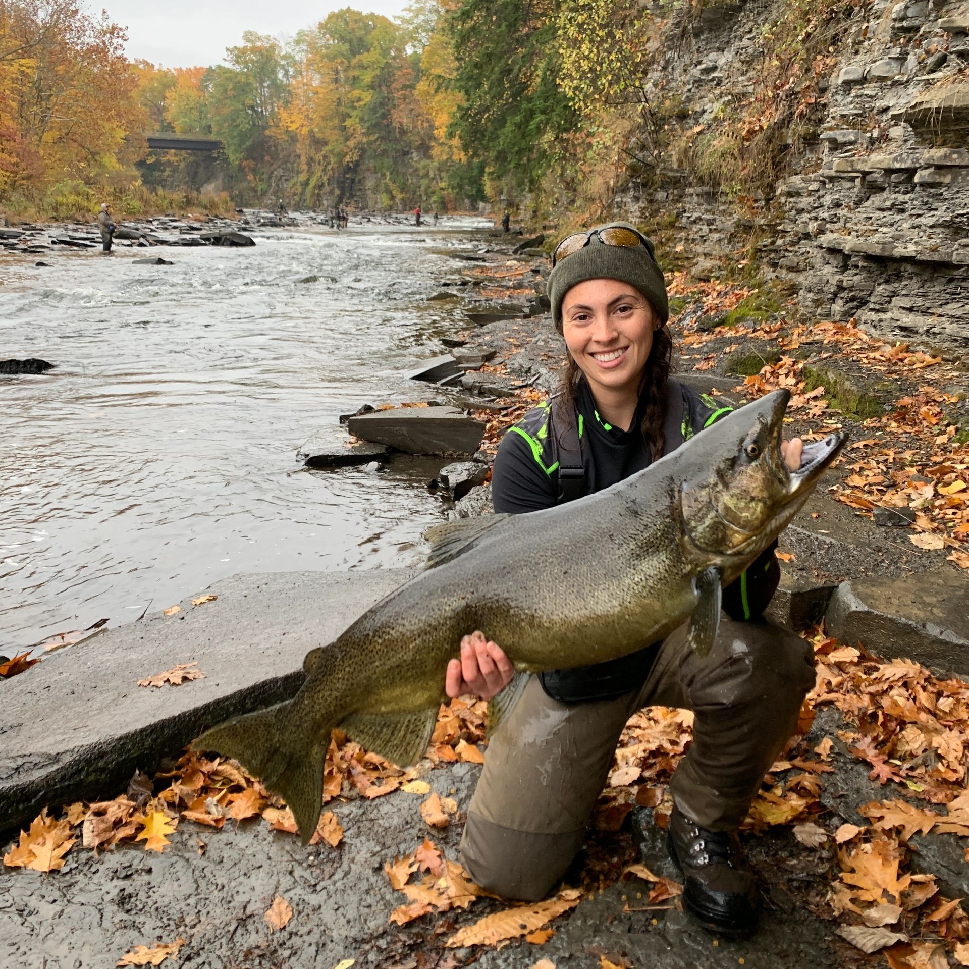 Woman (Zana) kneeling on the river's edge holding a 28 pound King salmon. 