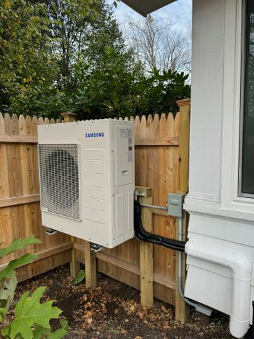Samsung outdoor HVAC unit mounted on a wooden fence in a backyard.