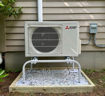 A Mitsubishi Electric air conditioning unit installed on a gravel bed outside a house.