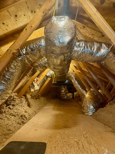Insulated HVAC ducts in an attic with wooden beams and insulation.