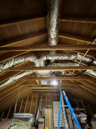 Attic with exposed wooden beams, insulated ductwork, and storage boxes.