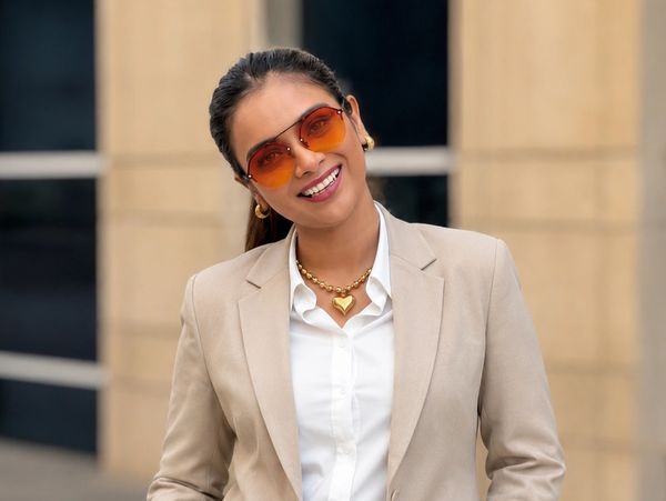 Woman in beige suit smiling confidently outdoors.