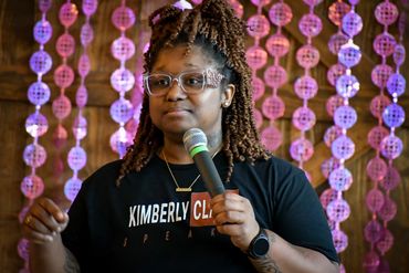 Woman speaking into a microphone with decorative purple lights in the background.