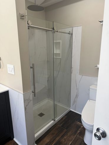 Modern bathroom with glass shower enclosure and wooden floor.