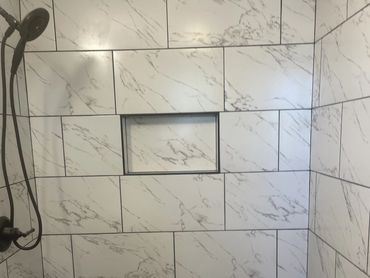 Modern shower with white marble tiles and a black showerhead.