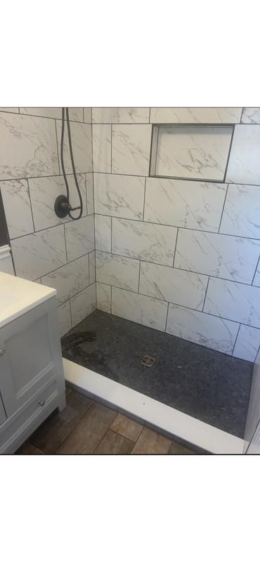 Modern shower with white marble tiles and a dark pebble floor.
