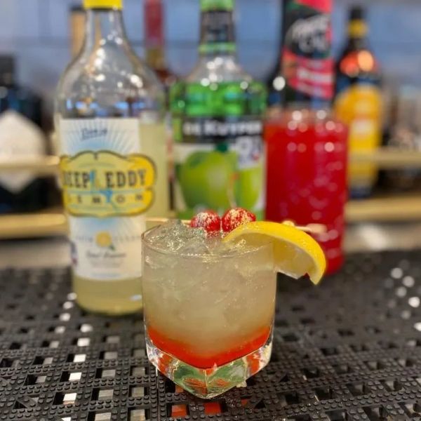 A refreshing cocktail with lemon garnish and cranberries on top.