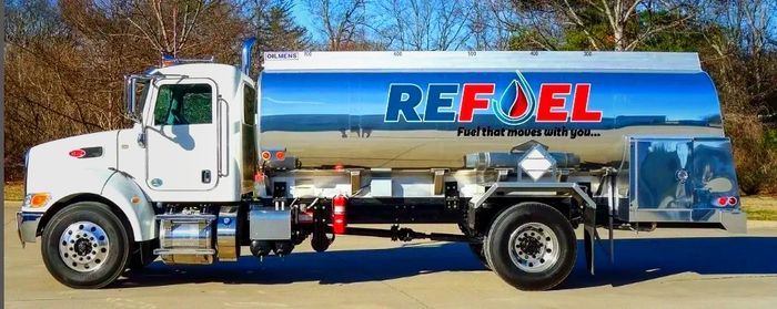 A white fuel tanker truck with 'REFUEL' branding parked outdoors.