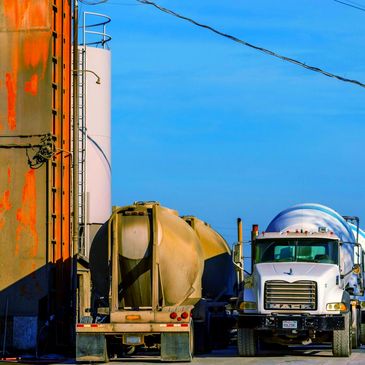 Concrete mixer trucks parked near an industrial building under a clear blue sky.