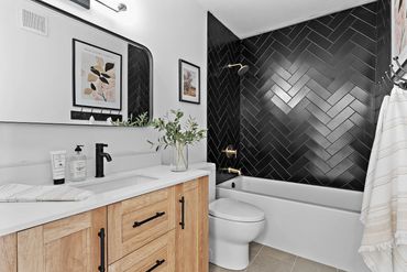 Black herringbone tile shower with light wood cabinet.