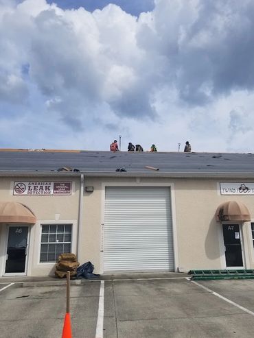 Workers on a commercial roof under a cloudy sky, repairing or inspecting.