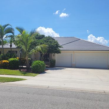 Suburban house with a three-car garage and tropical landscaping under a clear blue sky.