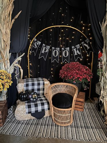 Cozy Halloween setup with hay bale seating, black pumpkins, and a spooky banner.