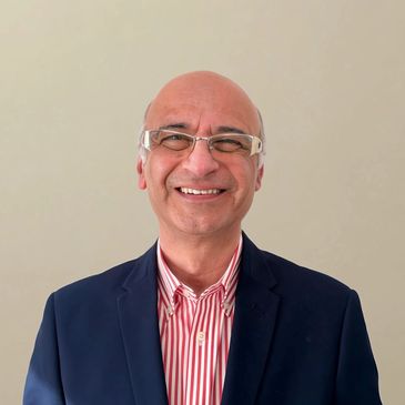Smiling man in glasses, striped shirt, and navy blazer against a plain background.