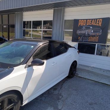 White car with black roof parked outside a Pro Dealer GeoShield shop.