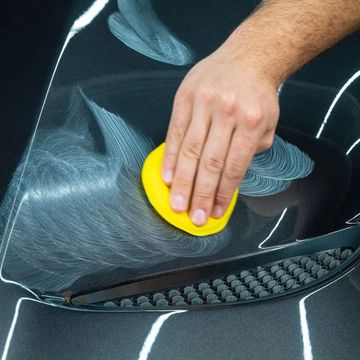 Hand applying polish on car surface with a yellow pad.