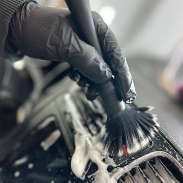 Hand in glove cleaning a car's interior with a brush.