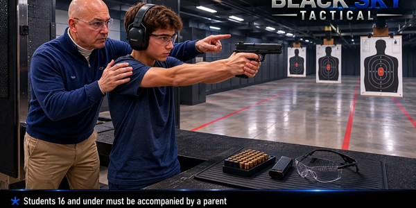 A coach instructs a young shooter at an indoor gun range with targets downrange.