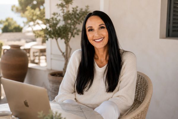 Smiling woman with long dark hair sitting at a table with a laptop.