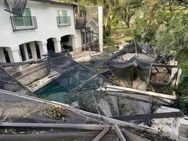 Damaged pool enclosure with torn screens near a white house.