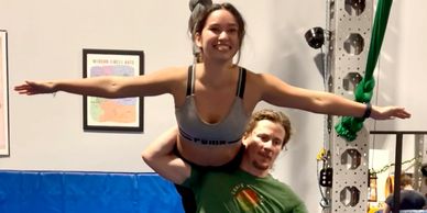 Two people performing an acrobatic balance pose indoors on a blue mat.