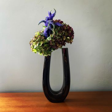 Ikebana floral arrangement in U shaped tall vase with green hydrangea and purple veronica
