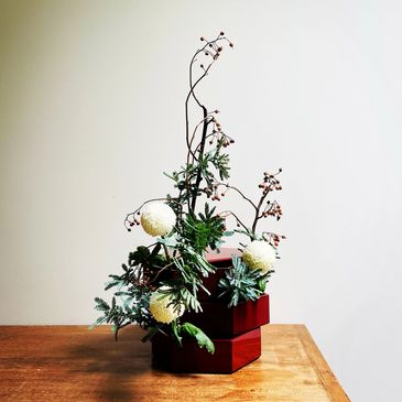 Ikebana installation in Japanese red lacquered container with chrysanthemum, wattle and rose hip