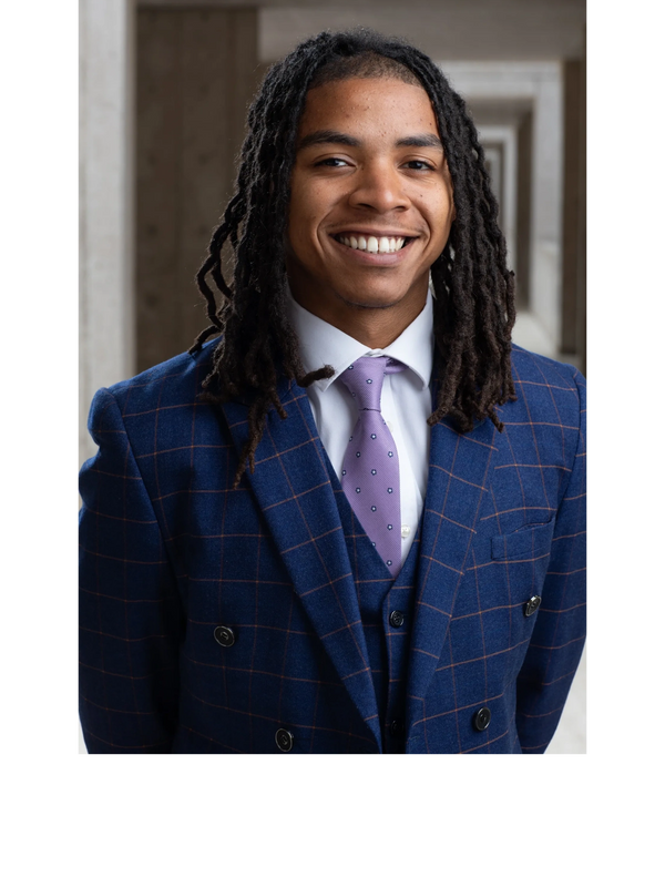 Young man in a blue checkered suit smiling confidently.