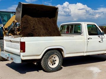 A white pickup truck is being loaded with soil by a loader.