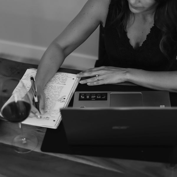 Annette Bruneau writing in her office, enjoying a glass of red wine.