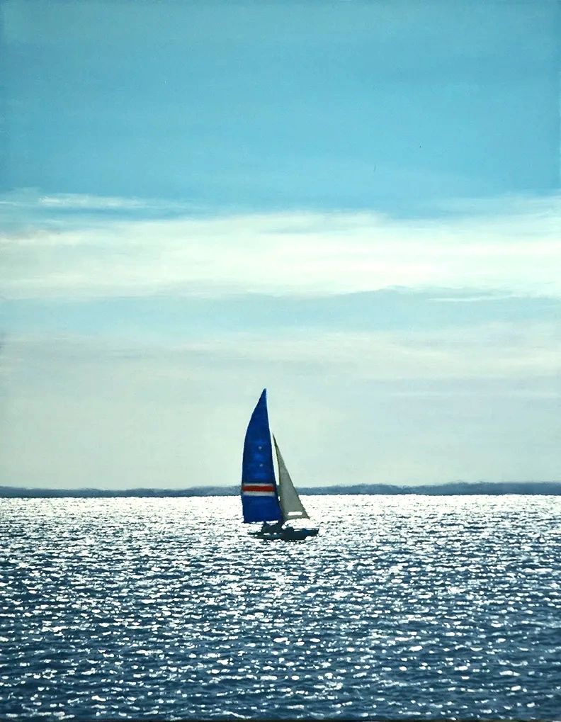 Blue and white boat with two sails nearly silhouetted against bright sunlight hitting the water. 