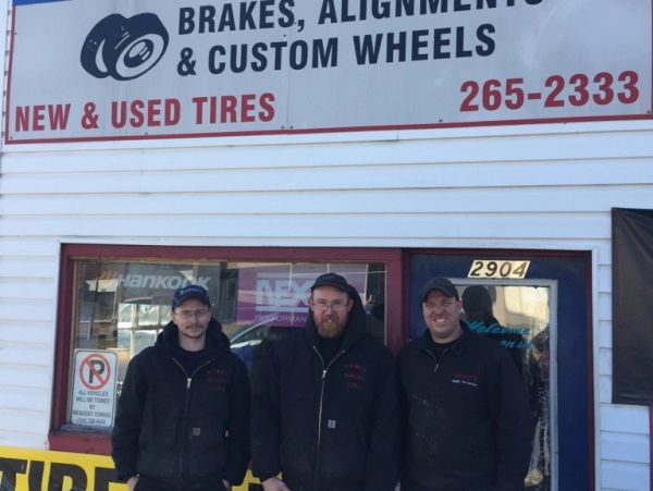 Three men standing outside a tire and wheel shop.